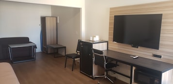 Una habitación de hotel con cama, escritorio, silla, televisor y armario.