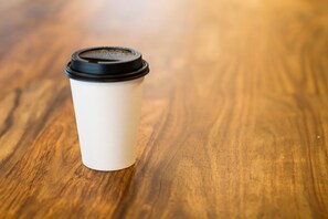 Une tasse à café blanche à usage unique, avec un couvercle noir, posée sur une surface en bois.