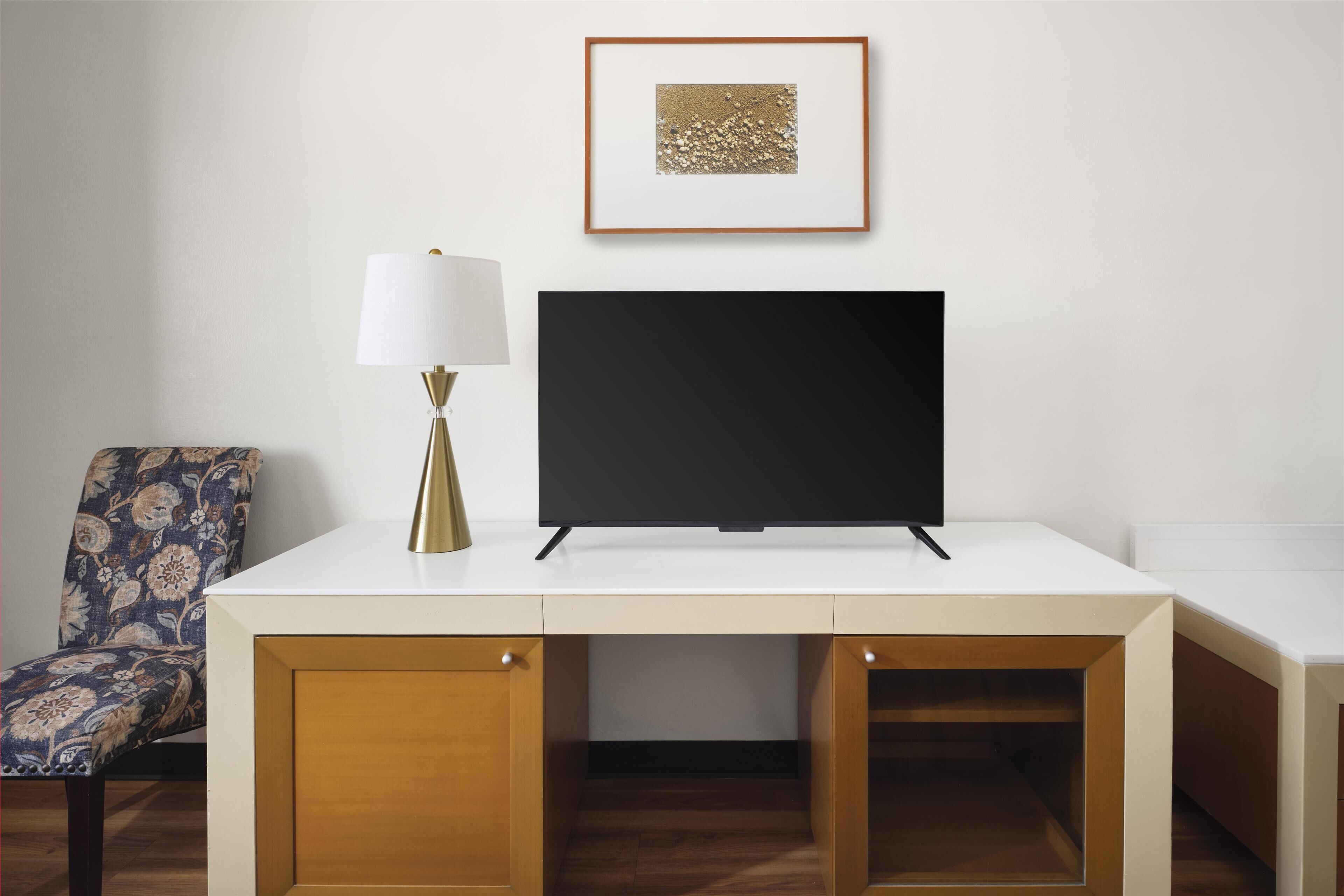 Een moderne kamer met een wit bureau, een televisie, een gestreept fauteuil en een lijst met een afbeelding aan de muur.