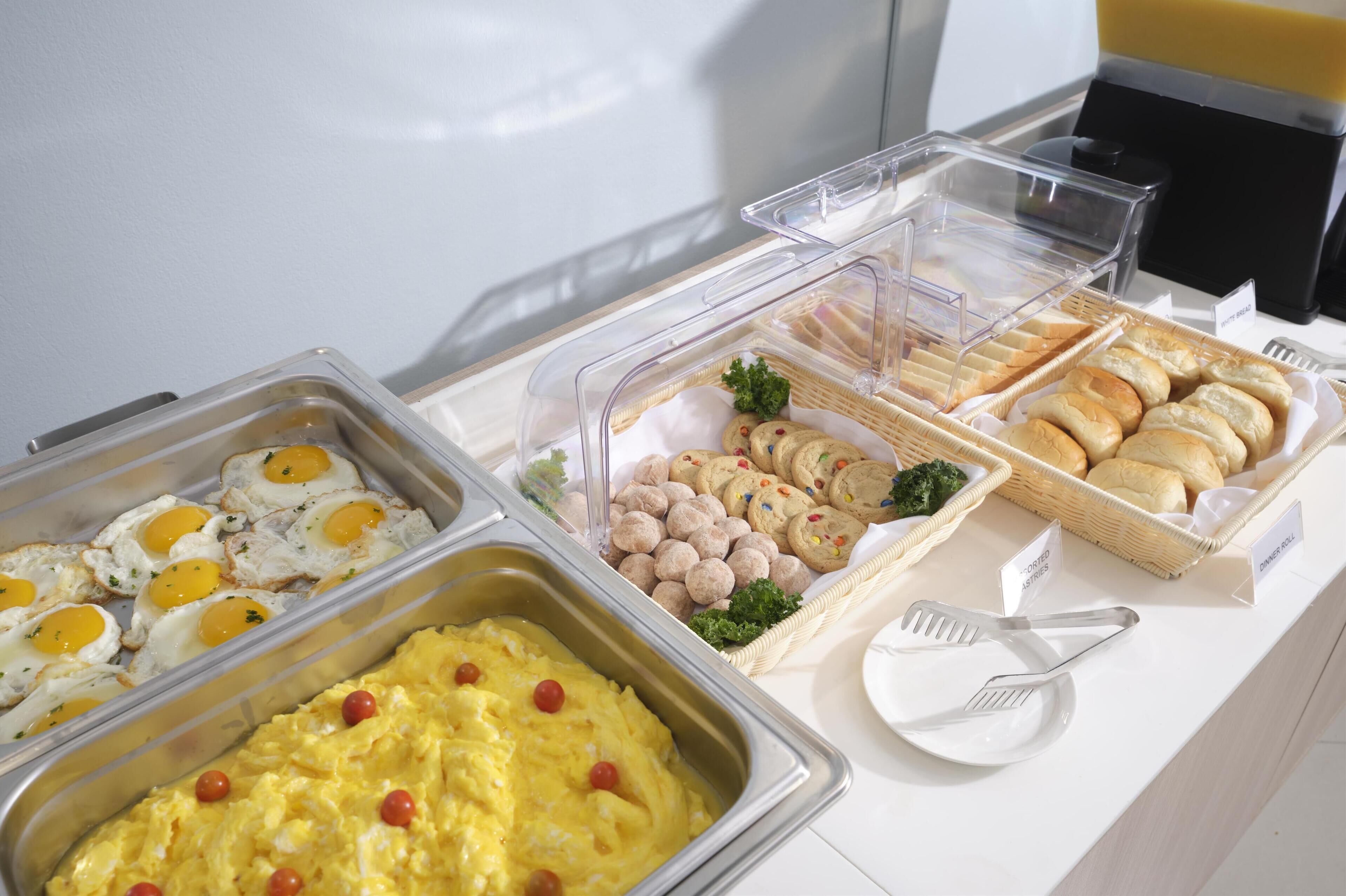 A buffet with various food items including eggs, scrambled eggs, muffins, and cookies.