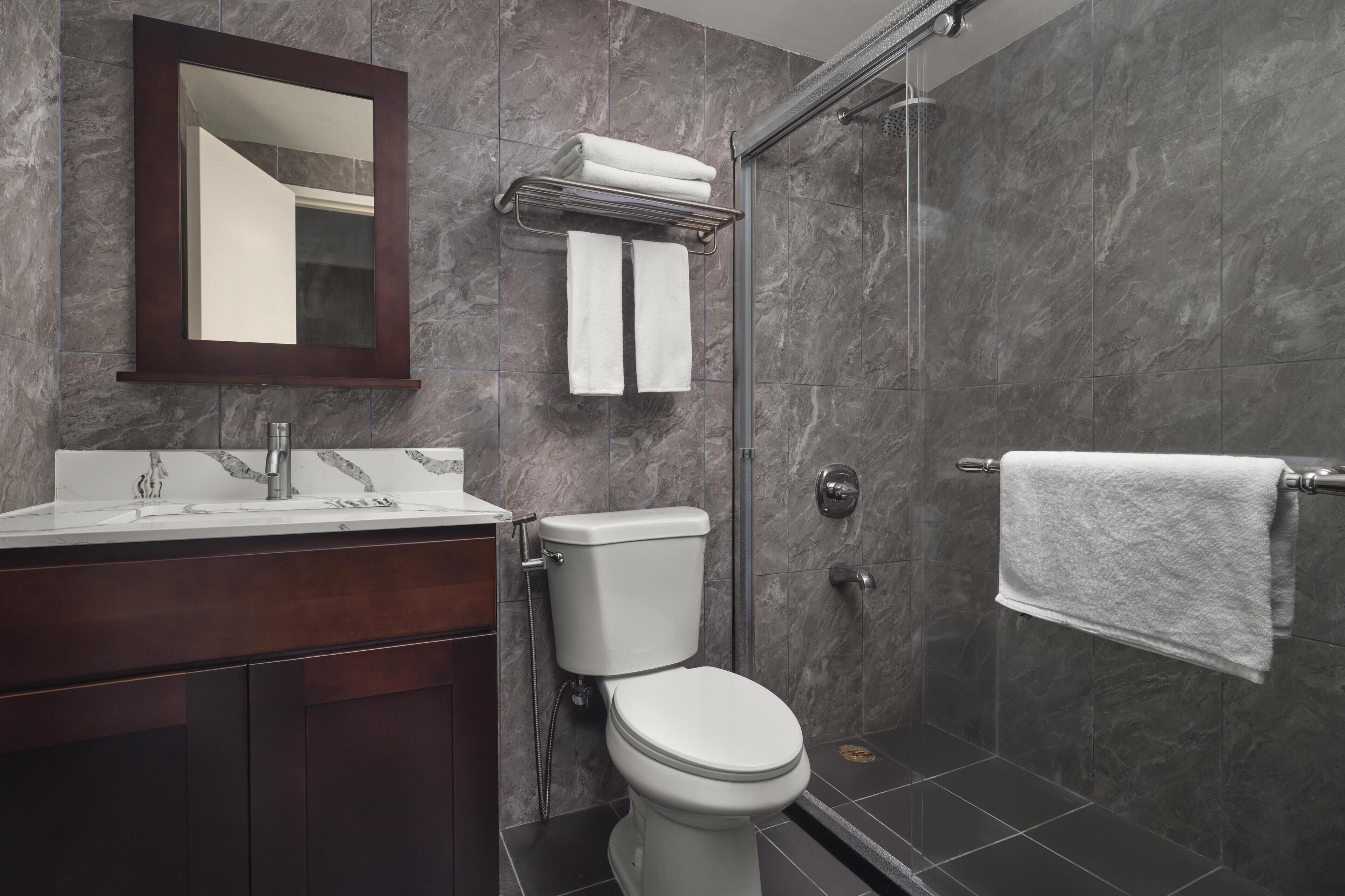 A modern bathroom with a marble wall, a glass shower enclosure, a white toilet, and a vanity with a mirror.