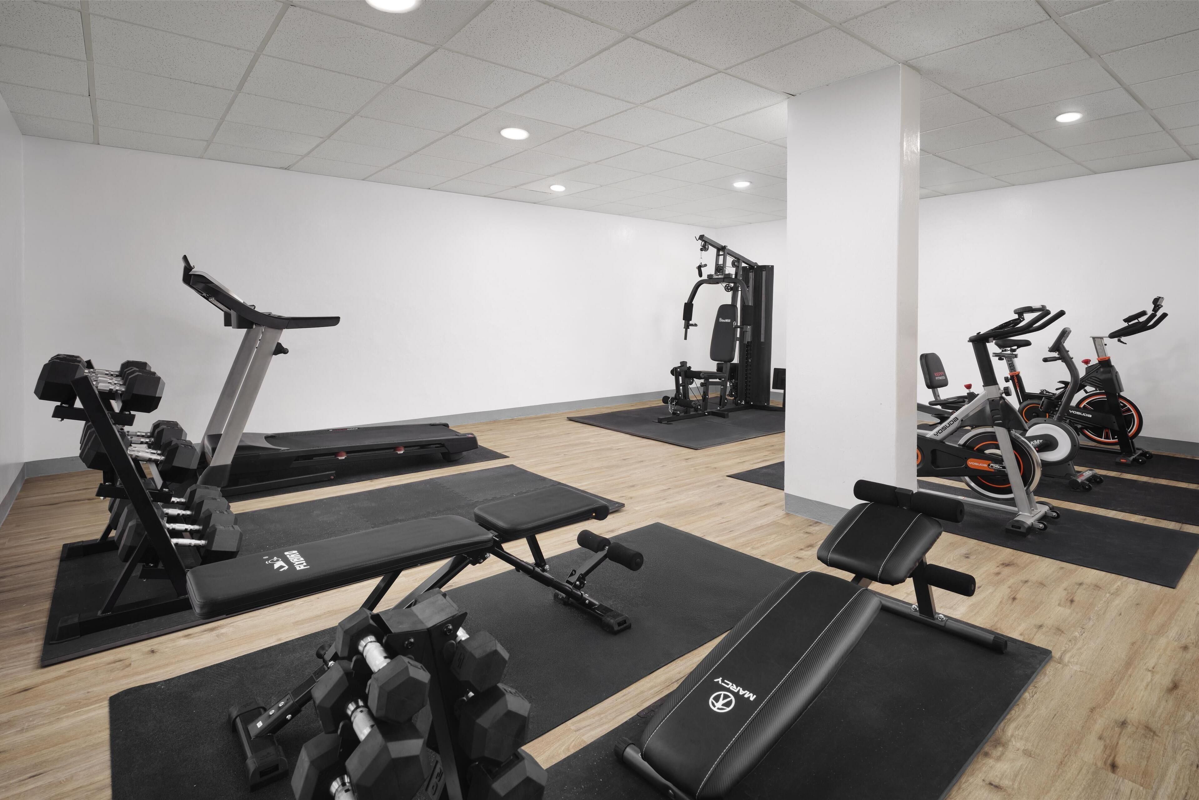 Une salle de sport équipée de divers appareils d’exercice, notamment des tapis de course, des bancs de musculation et des haltères.