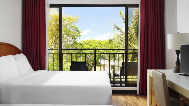 A hotel room with a large bed, a desk, and a balcony with a view of greenery and trees. - SureStay Hotel by Best Western Guam Airport South (Barrigada)