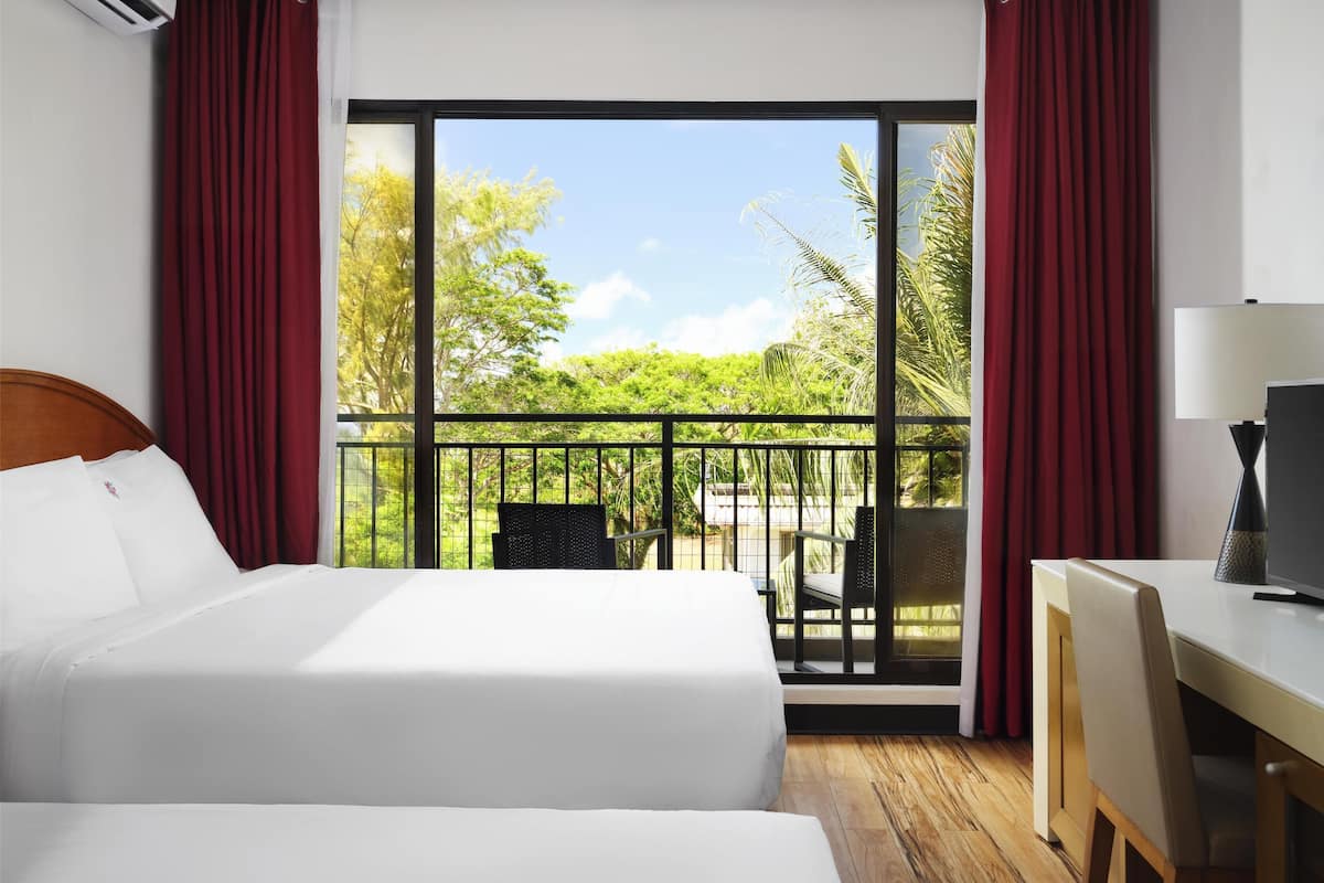 Ein Hotelzimmer mit einem großen Bett, einem Schreibtisch und einem Balkon mit Blick auf Grünflächen und Bäume.