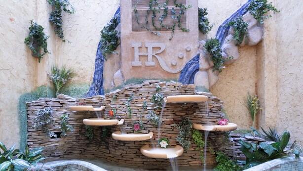 A stone water feature with cascading water, surrounded by plants and a wall with the letters "HR". - Hotel Real Lleida (Lleida)