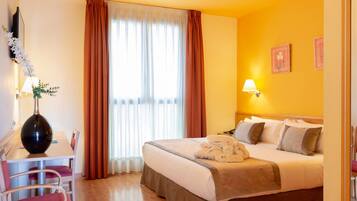 A hotel room with a bed, bedside table, lamp, and a desk with a chair.