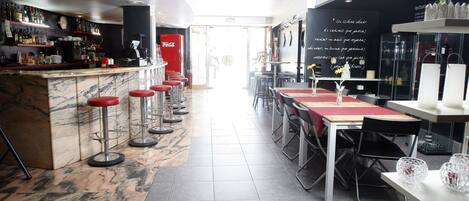 A bar area with a marble counter, red bar stools, and a red Coca-Cola refrigerator. There are tables with chairs and a blackboard with writing.