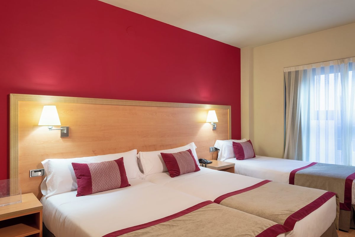 Une chambre d’hôtel avec deux lits, des murs rouges et une fenêtre avec des rideaux.