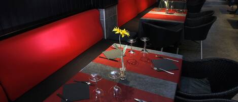 Un restaurante con asientos tapizados en rojo y mesas dispuestas con copas de vino, cubiertos y servilletas.