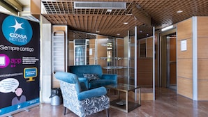 A modern hotel lobby with a blue armchair, a glass table, and a promotional poster for EIZASA HOTELS. - Hotel Real Lleida (Lleida)