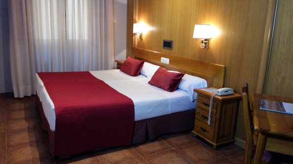 A hotel room with a large bed, two bedside lamps, a wooden nightstand, and a chair.
