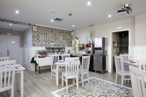 Una cocina moderna con armarios blancos, horno empotrado y refrigerador. Hay sillas blancas alrededor de una mesa con alfombra estampada.