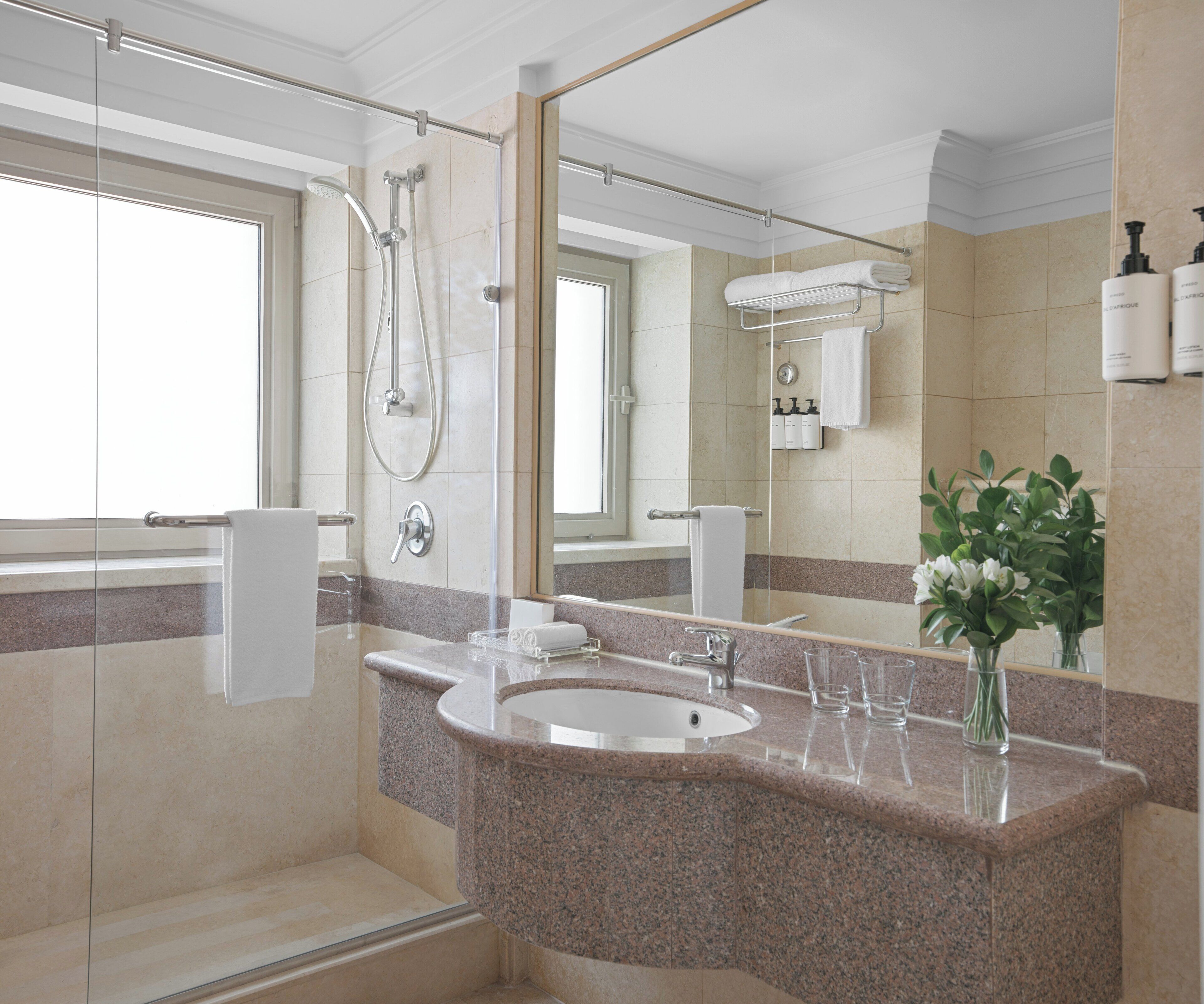 Un baño moderno con encimera de granito, ducha con mampara de vidrio y un espejo grande.