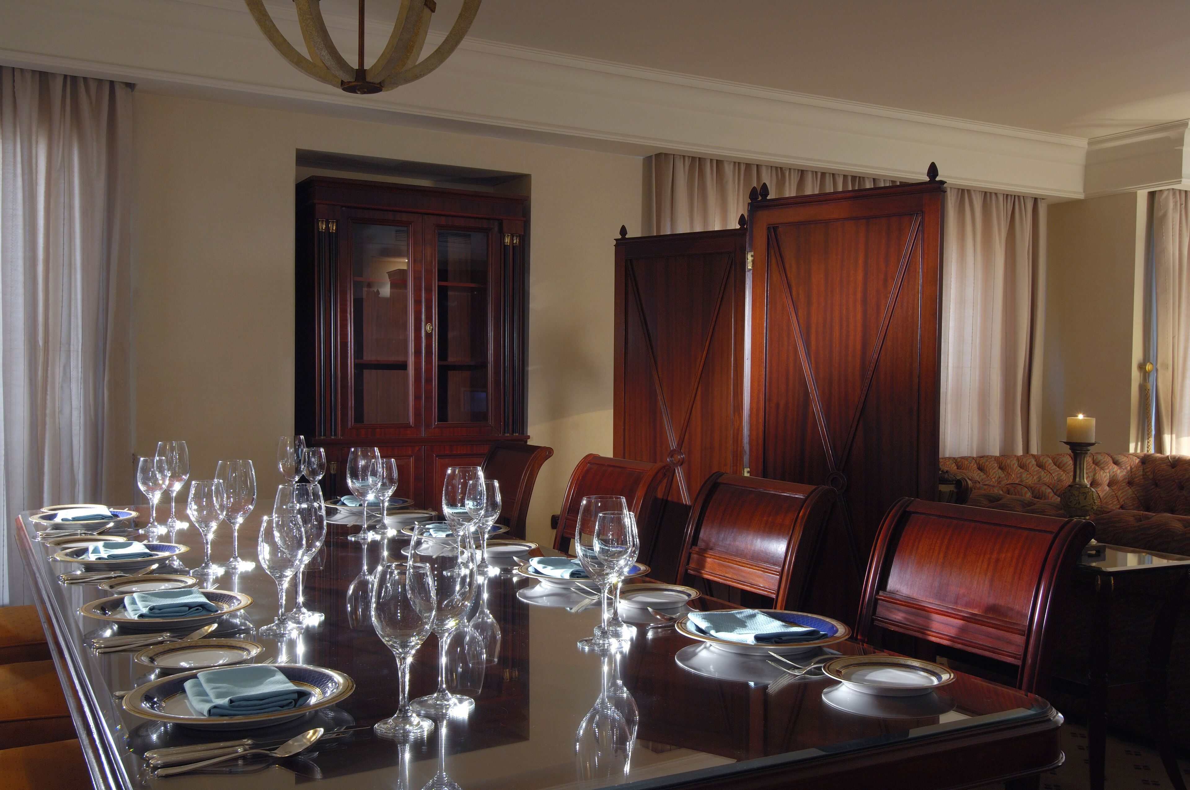 A formal dining room with a long table set for a meal, wooden chairs, and a sofa in the background.