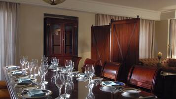 A formal dining room with a long table set for a meal, wooden chairs, and a sofa in the background.