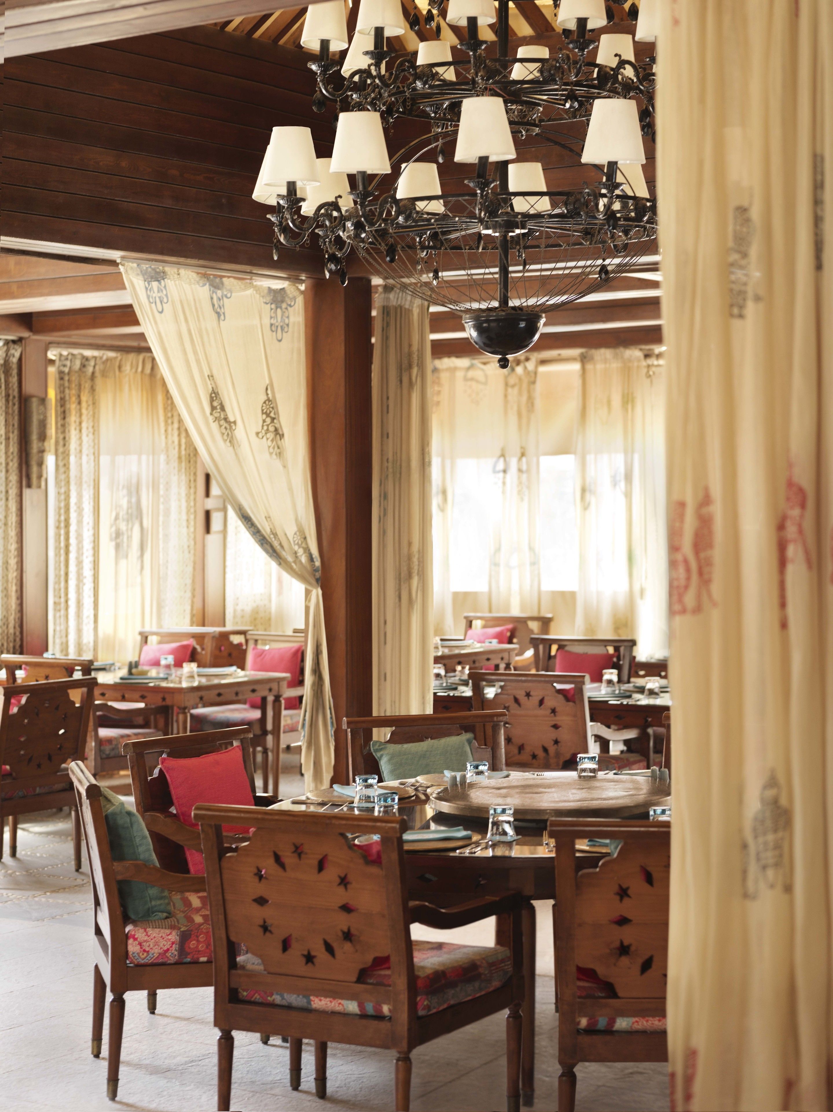 A traditional dining area with wooden tables and chairs, a chandelier, and curtains.