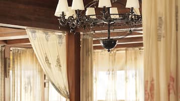 A traditional dining area with wooden tables and chairs, a chandelier, and curtains.