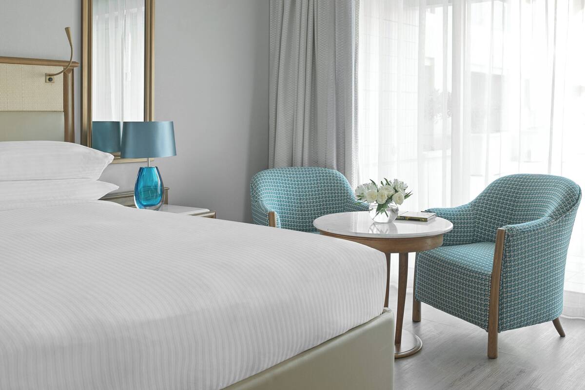 A hotel room with a large bed, two chairs, a small table, and a lamp.