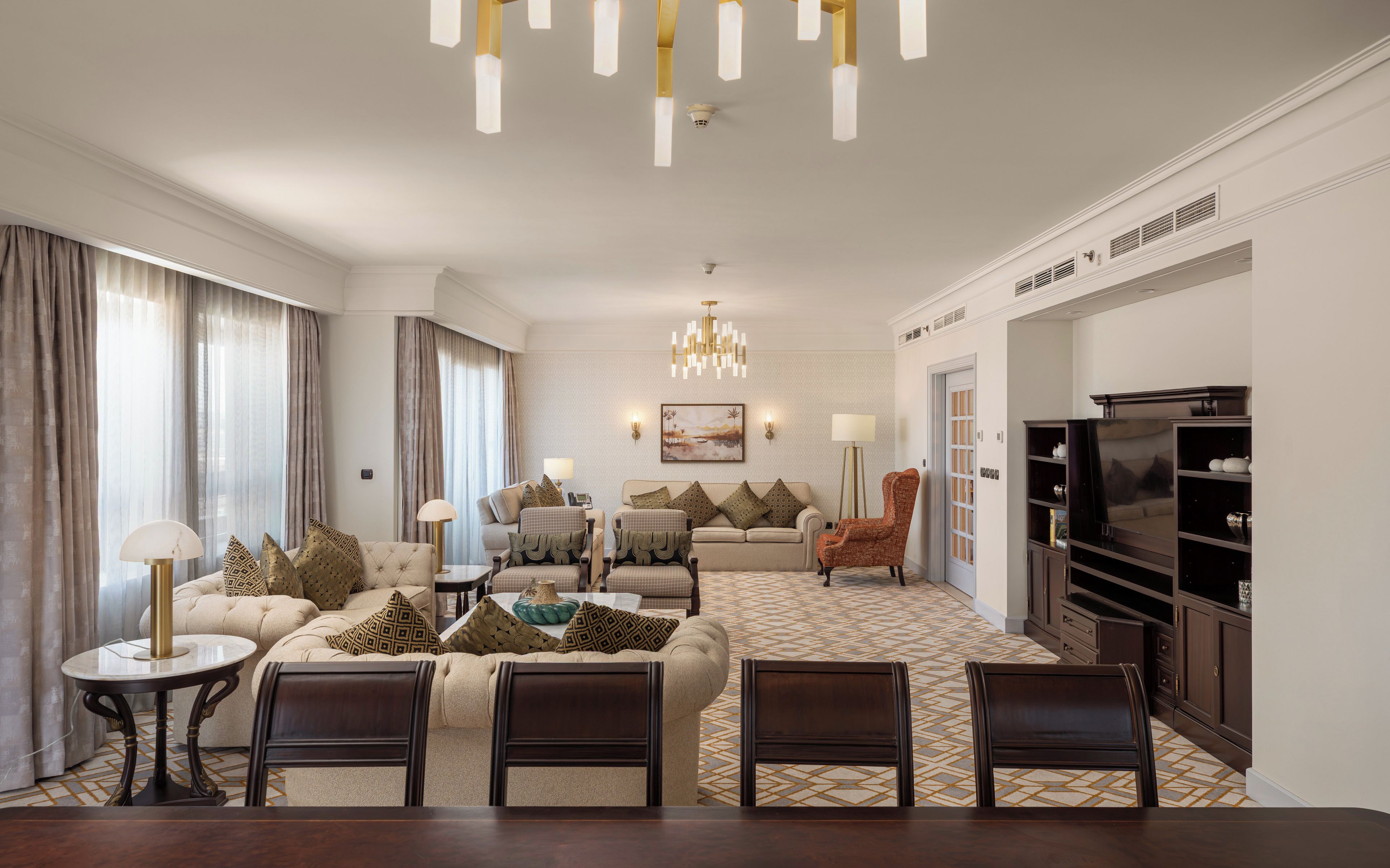 A spacious living room with a sofa set, a dining table with chairs, a television, and a chandelier.