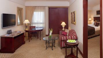 Habitación de hotel con televisión, una mesa de comedor, sofá, una mesita redonda con manzanas y una cama con almohadas.