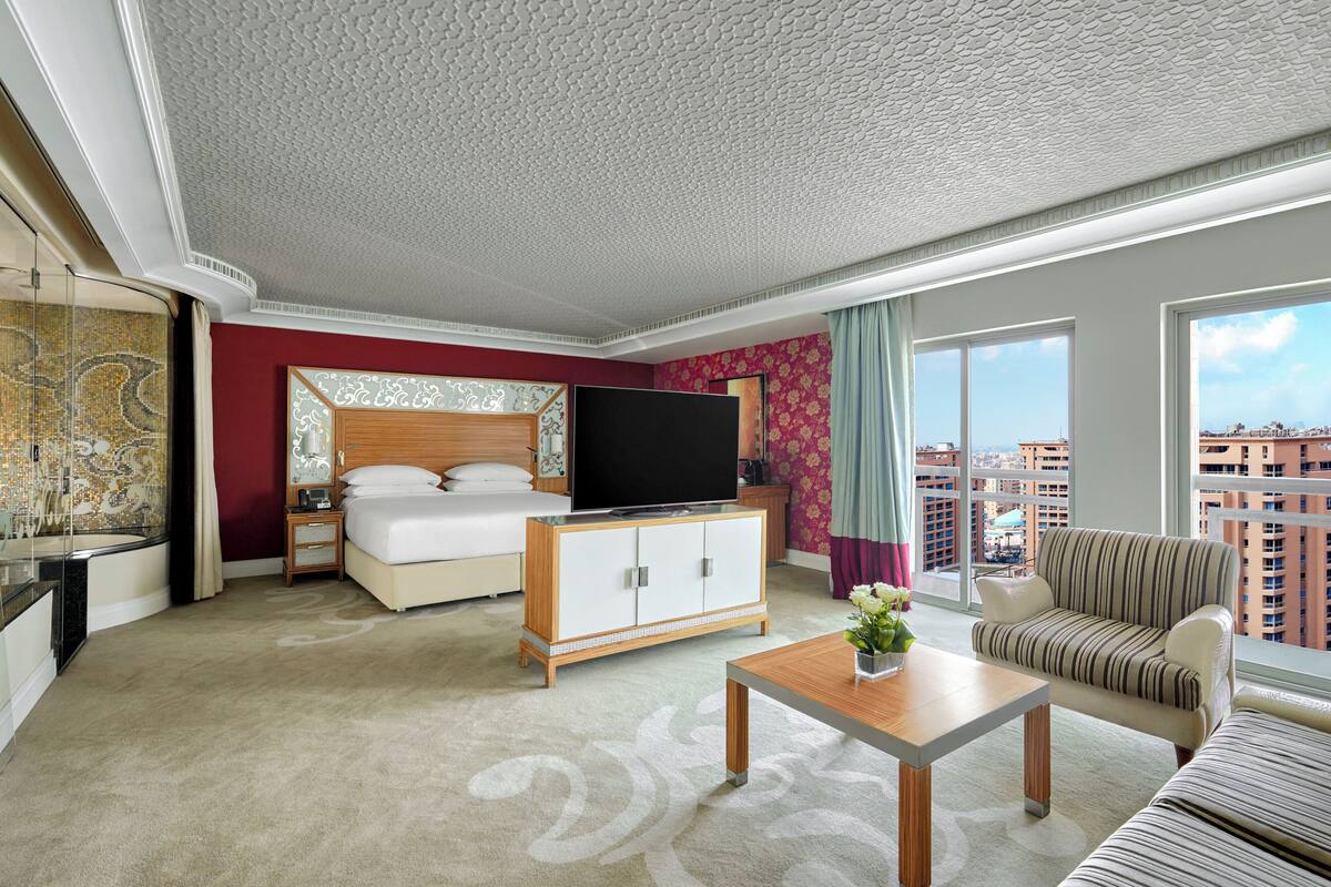 A hotel room with a bed, a TV, a sofa, a coffee table, and a view of the city.