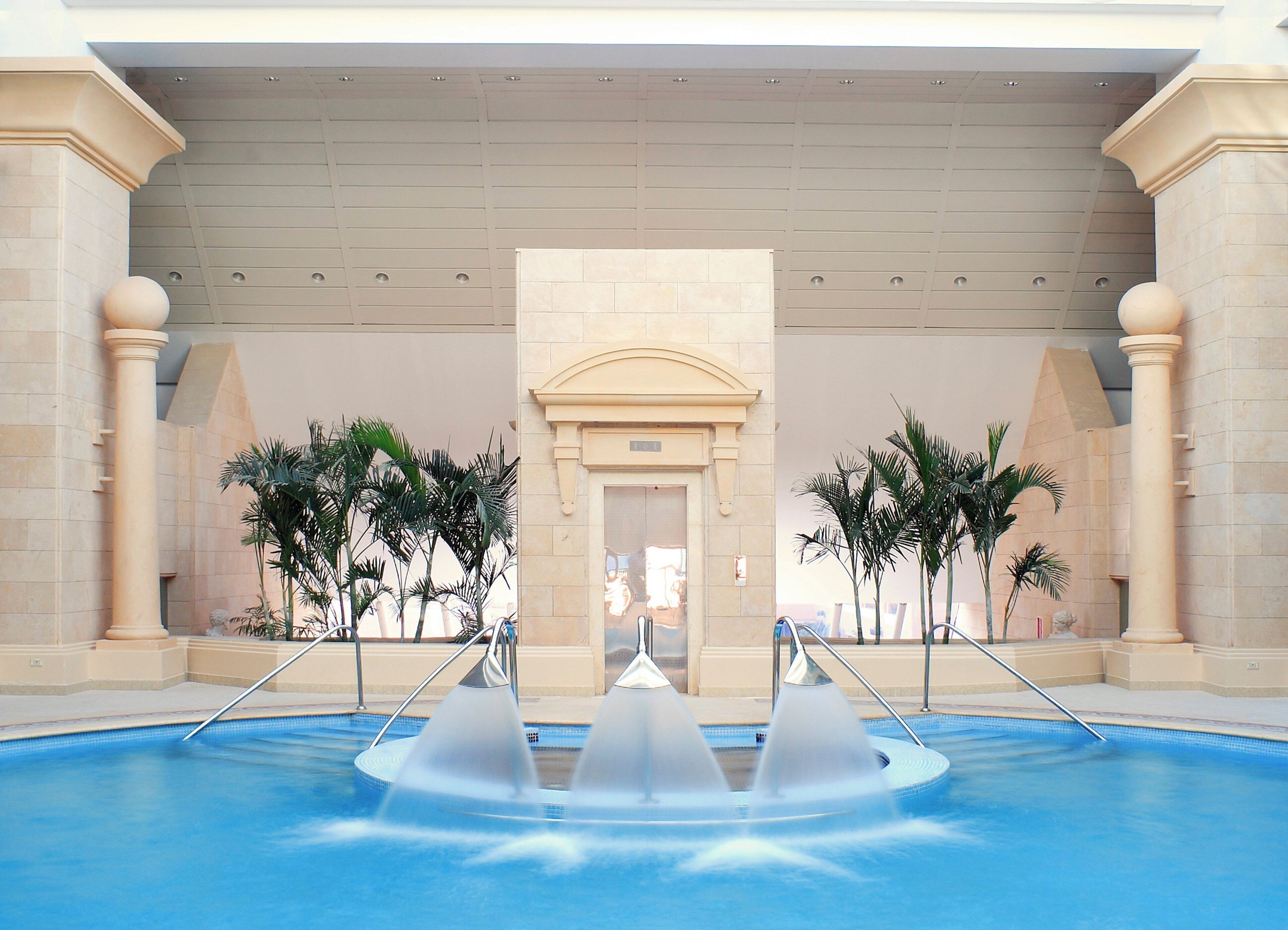 A pool area with a central water feature, palm trees, and classical architecture.