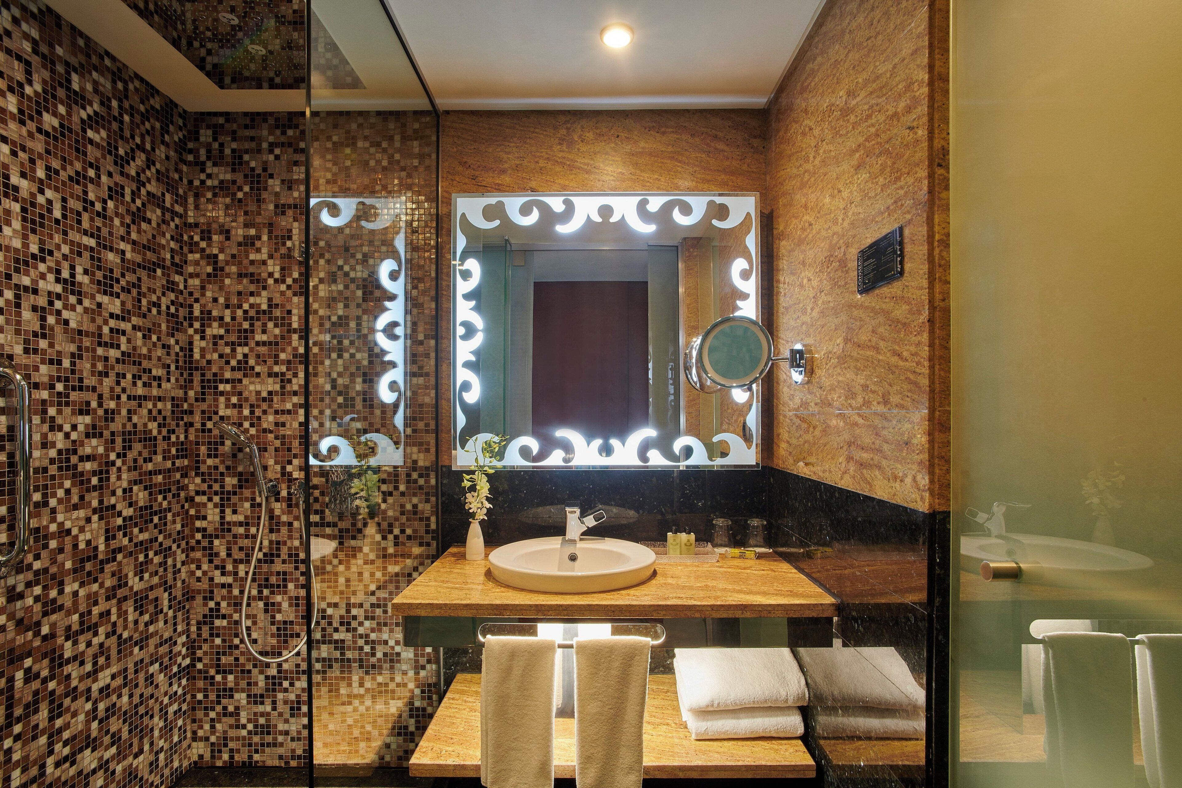 Une salle de bain avec un mur recouvert de mosaïques, un lavabo avec un miroir et un porte-serviettes.