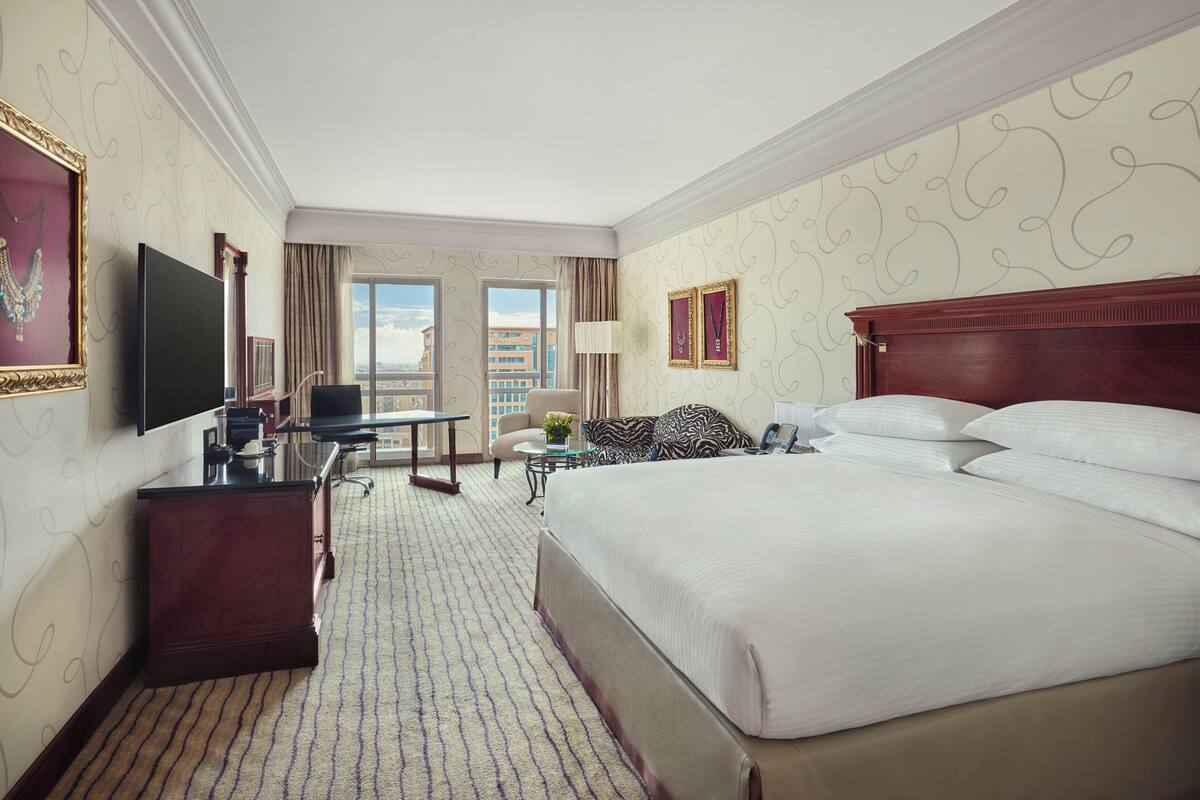 A hotel room with a large bed, a desk with a computer, a TV, and a view of the city.