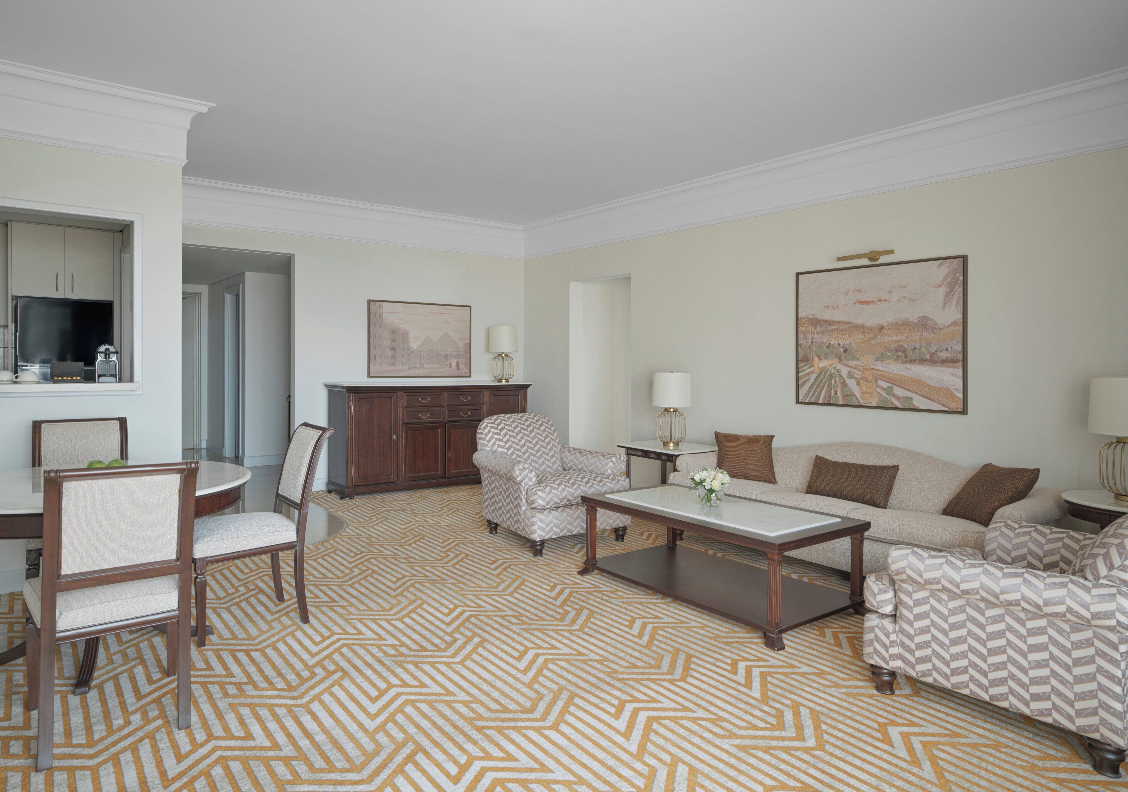 A living room with a herringbone patterned carpet, a sofa set, a coffee table, and a dining area with chairs and a table.