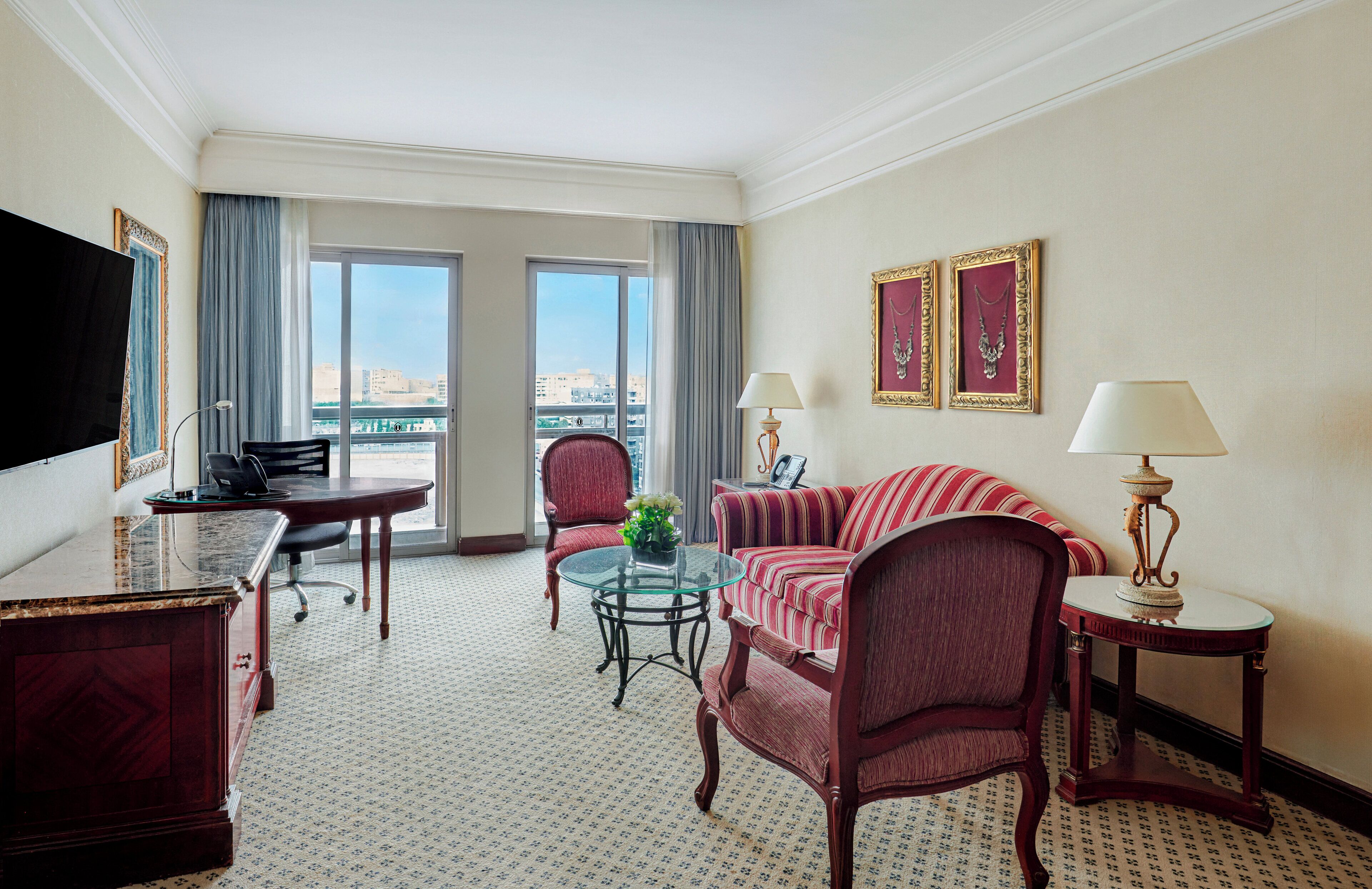 A hotel room with a large window, a sofa, a chair, a desk, and a television.