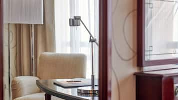 A hotel room with a round table, a chair, a lamp, and a window with curtains.