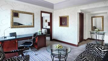A hotel room with a desk, office chair, zebra-patterned sofa, and a glass coffee table.