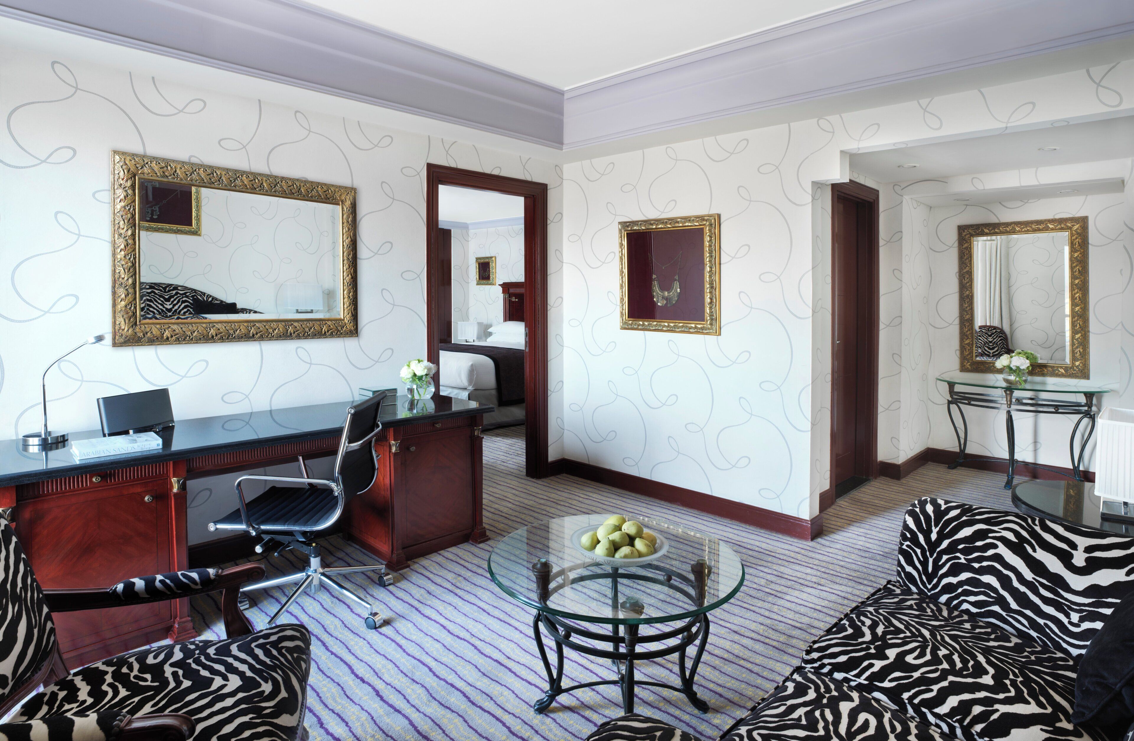 A hotel room with a zebra-patterned sofa, a desk with a computer, a glass coffee table, and two large mirrors on the walls.