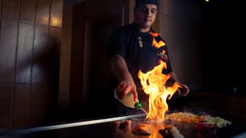 Un chef cuisinant des aliments sur un gril à l’aide de flammes.
