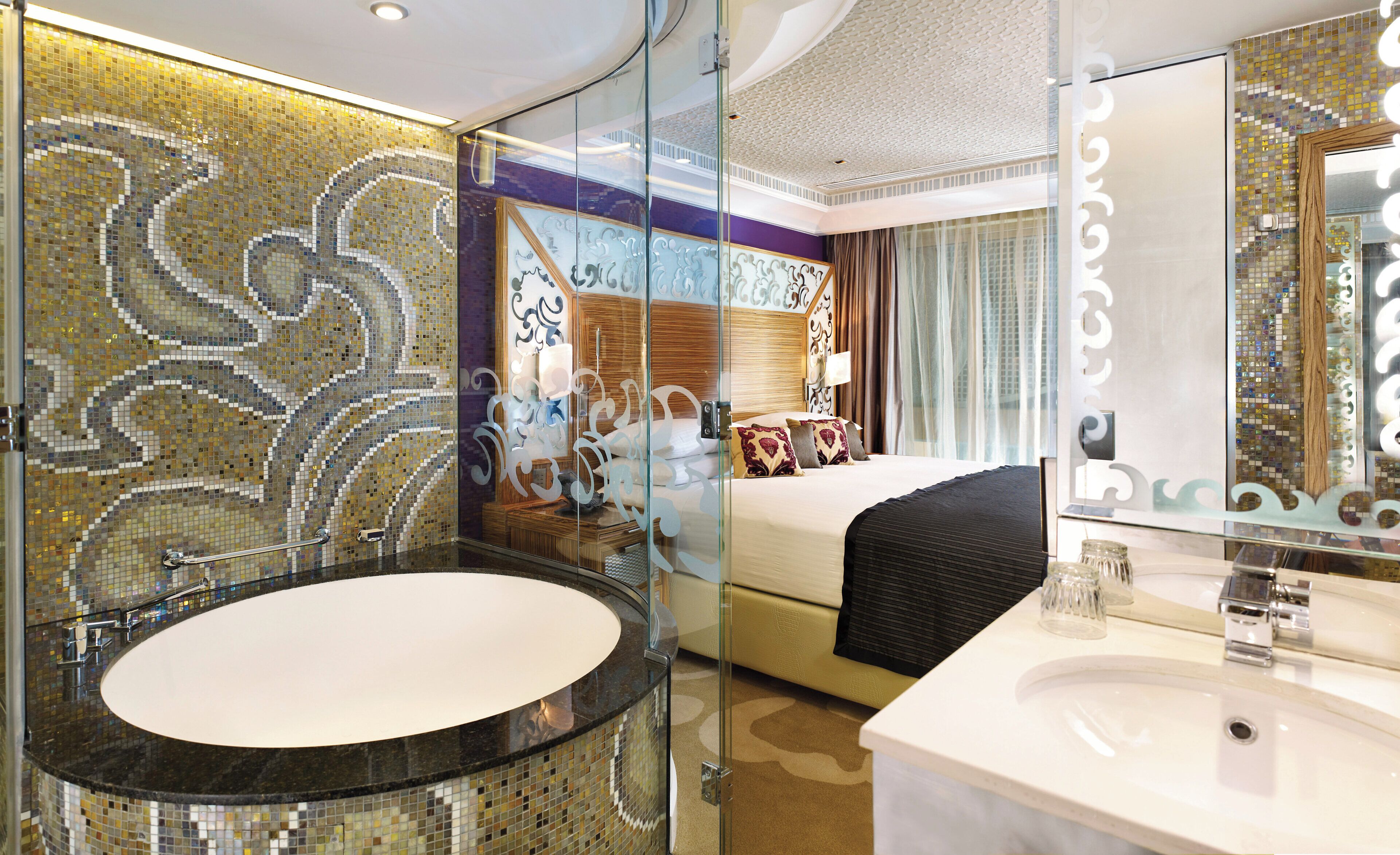 Une chambre d’hôtel dotée d’une grande baignoire ovale, d’un meuble-lavabo séparé avec un évier, d’un lit agrémenté de coussins décoratifs et d’un grand miroir.