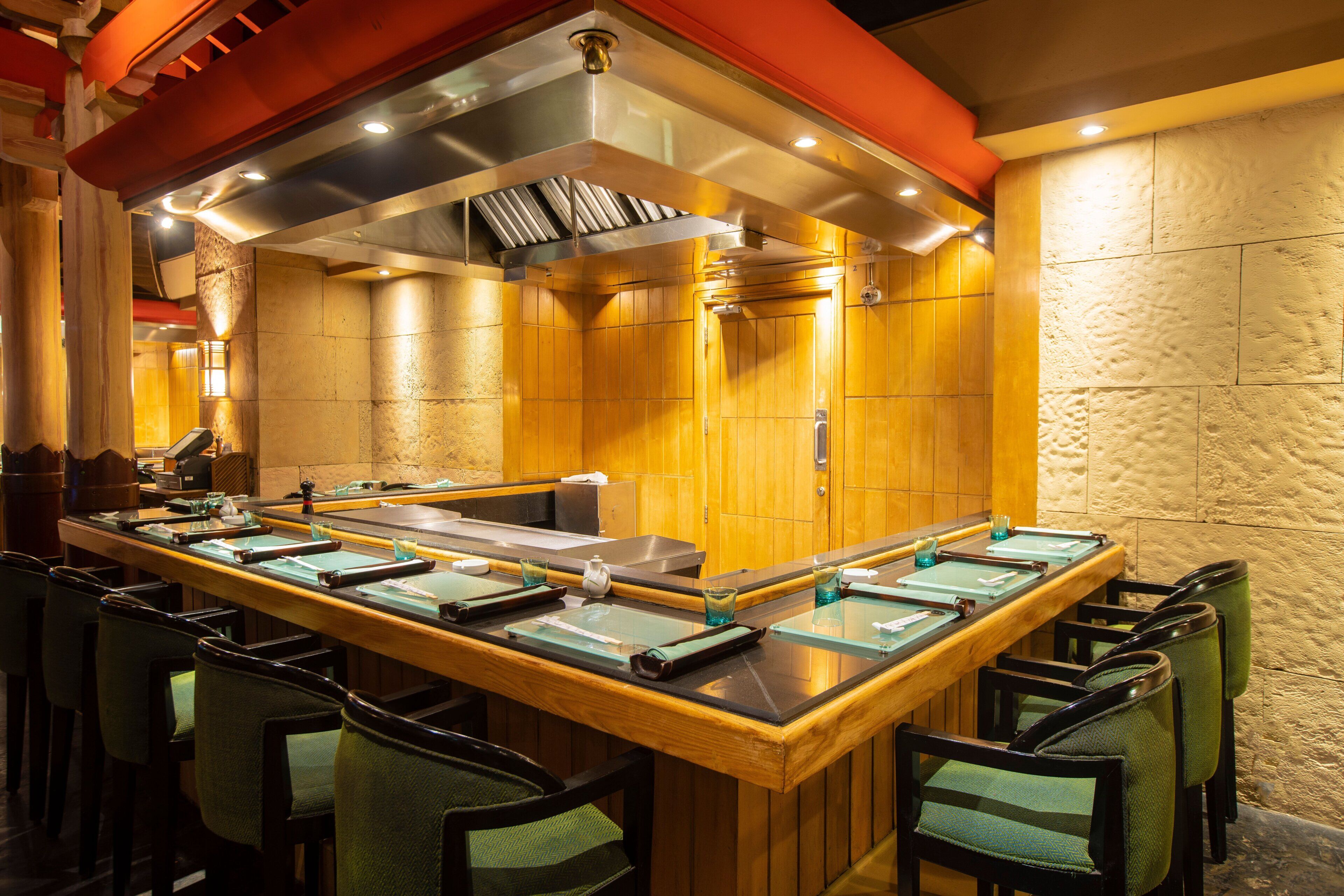 Un restaurante con una barra larga, múltiples sillas y una cocina moderna.