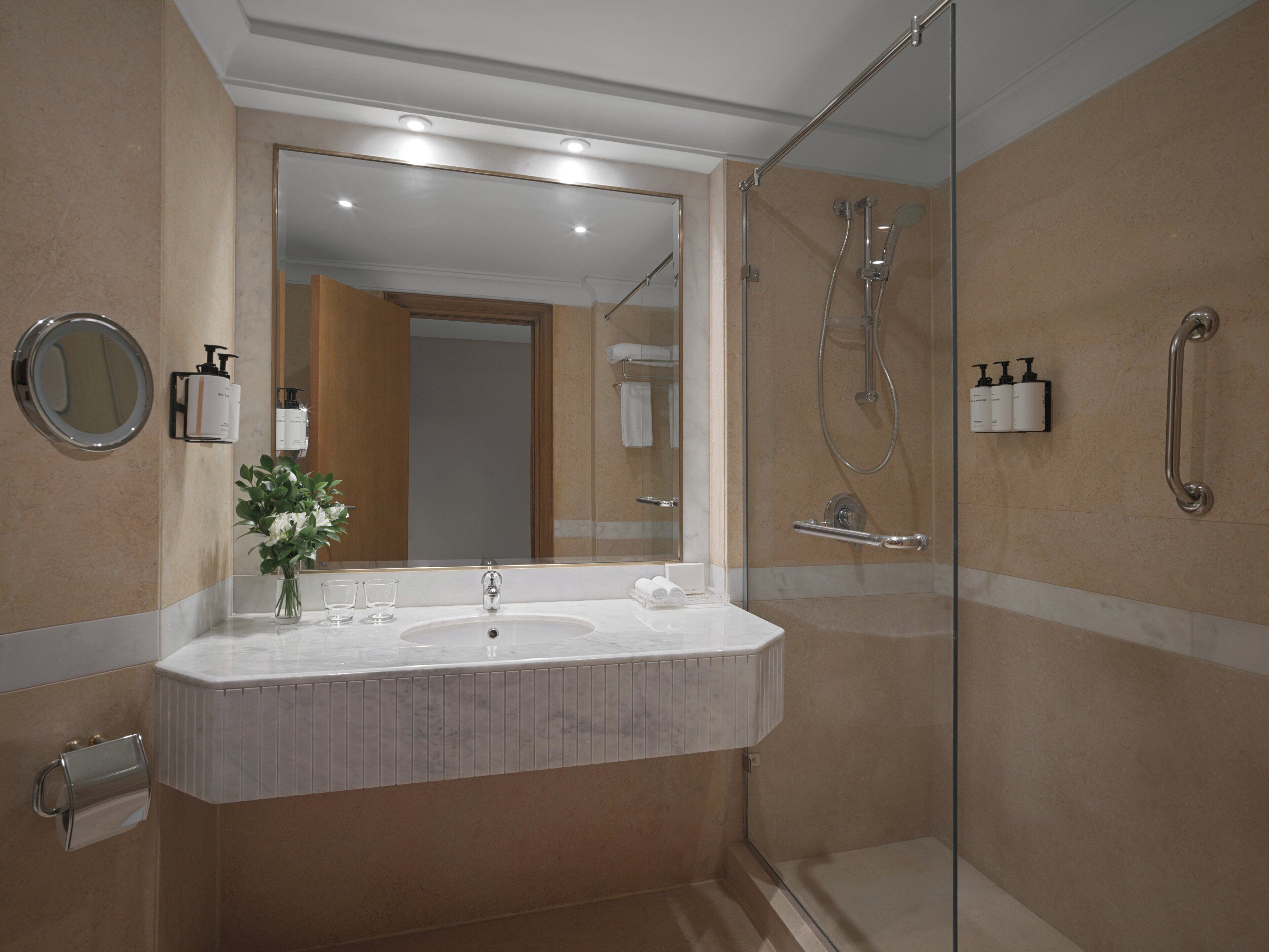 A modern bathroom with a large mirror, a sink, and a glass-enclosed shower.