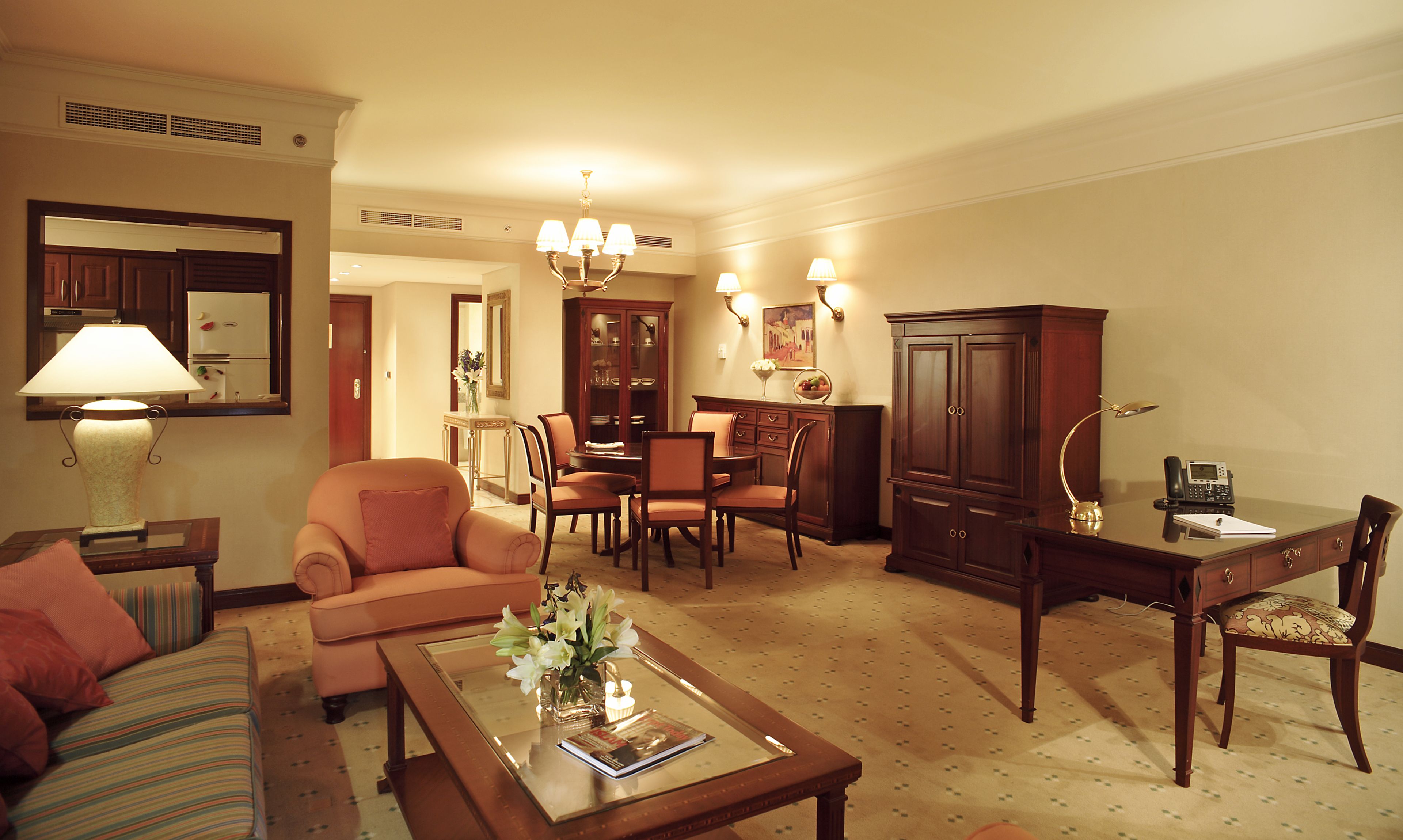 A well-lit living room with a sofa, armchair, dining table, and a cabinet.
