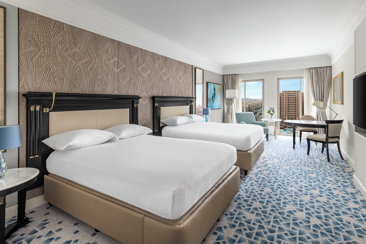 A hotel room with two beds, a desk, a chair, and a TV.