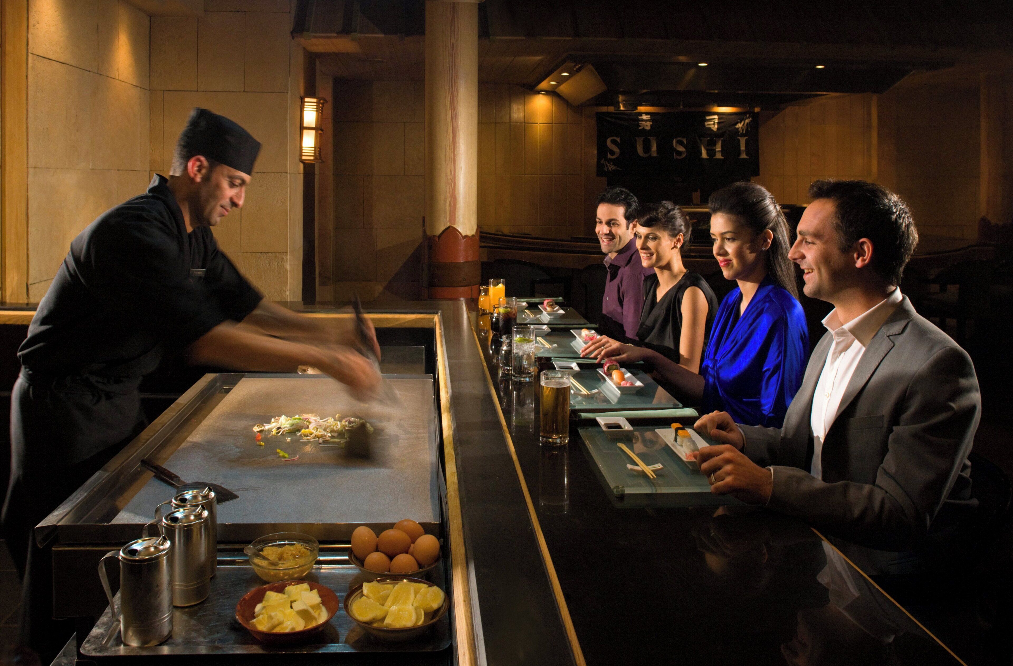 Een restaurantinterieur met een sushi-bar en een groep etende gasten.