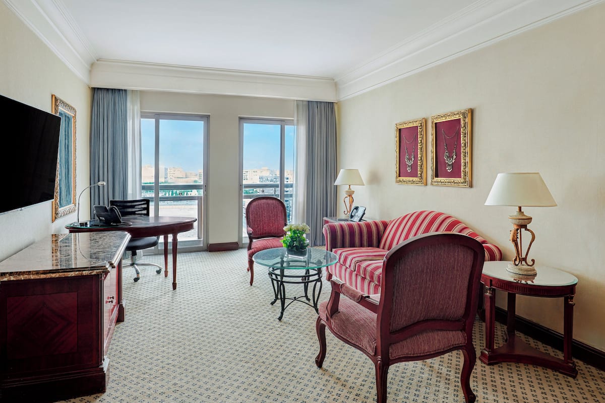 A hotel room with a large window, a sofa, a chair, a desk, and a television.