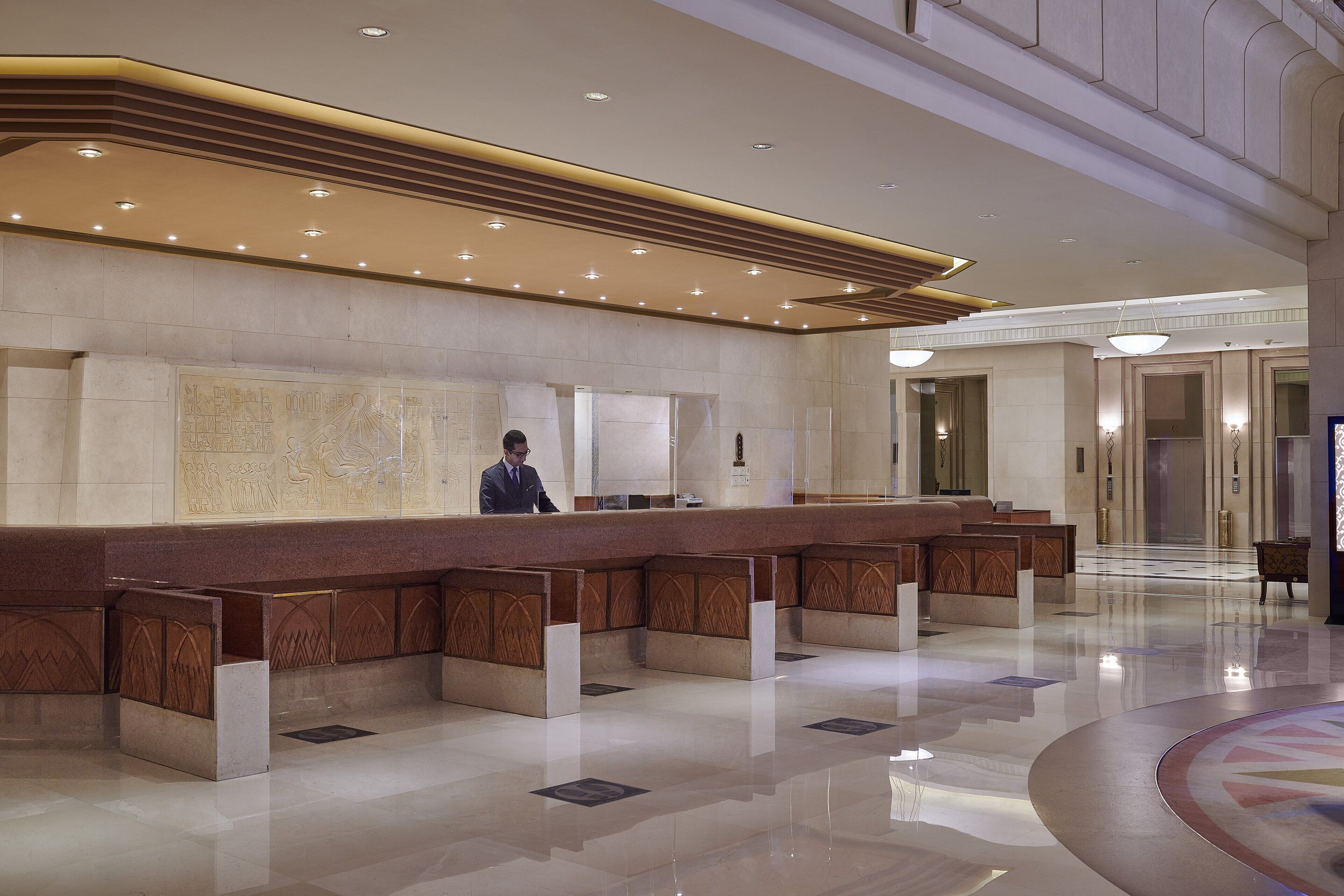 Ein Hotel-Rezeptionsbereich mit einer langen Theke, einer Rezeptionistin und einer großen Wanddekoration.