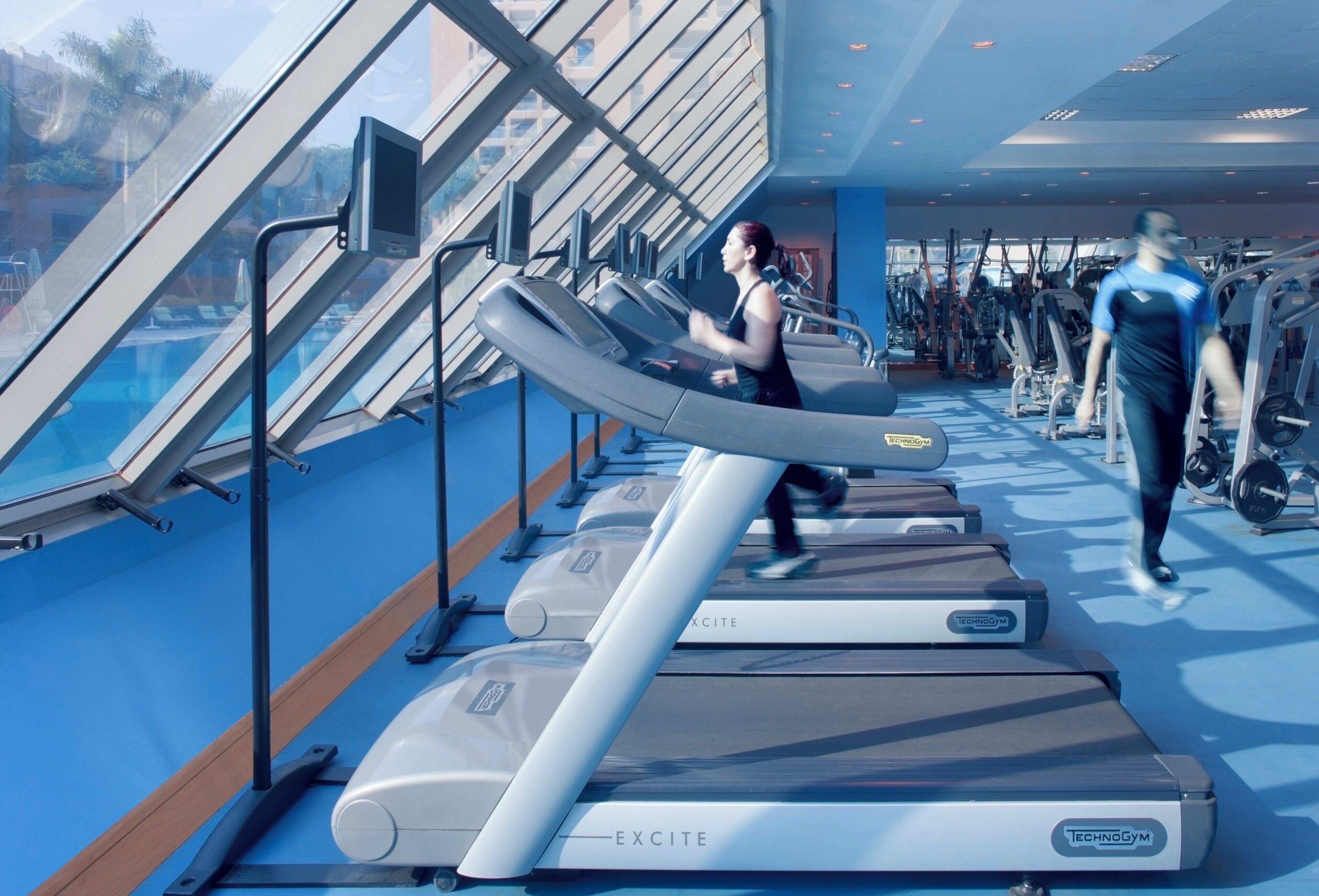 A gym with treadmills, weight machines, and a large window overlooking a pool.