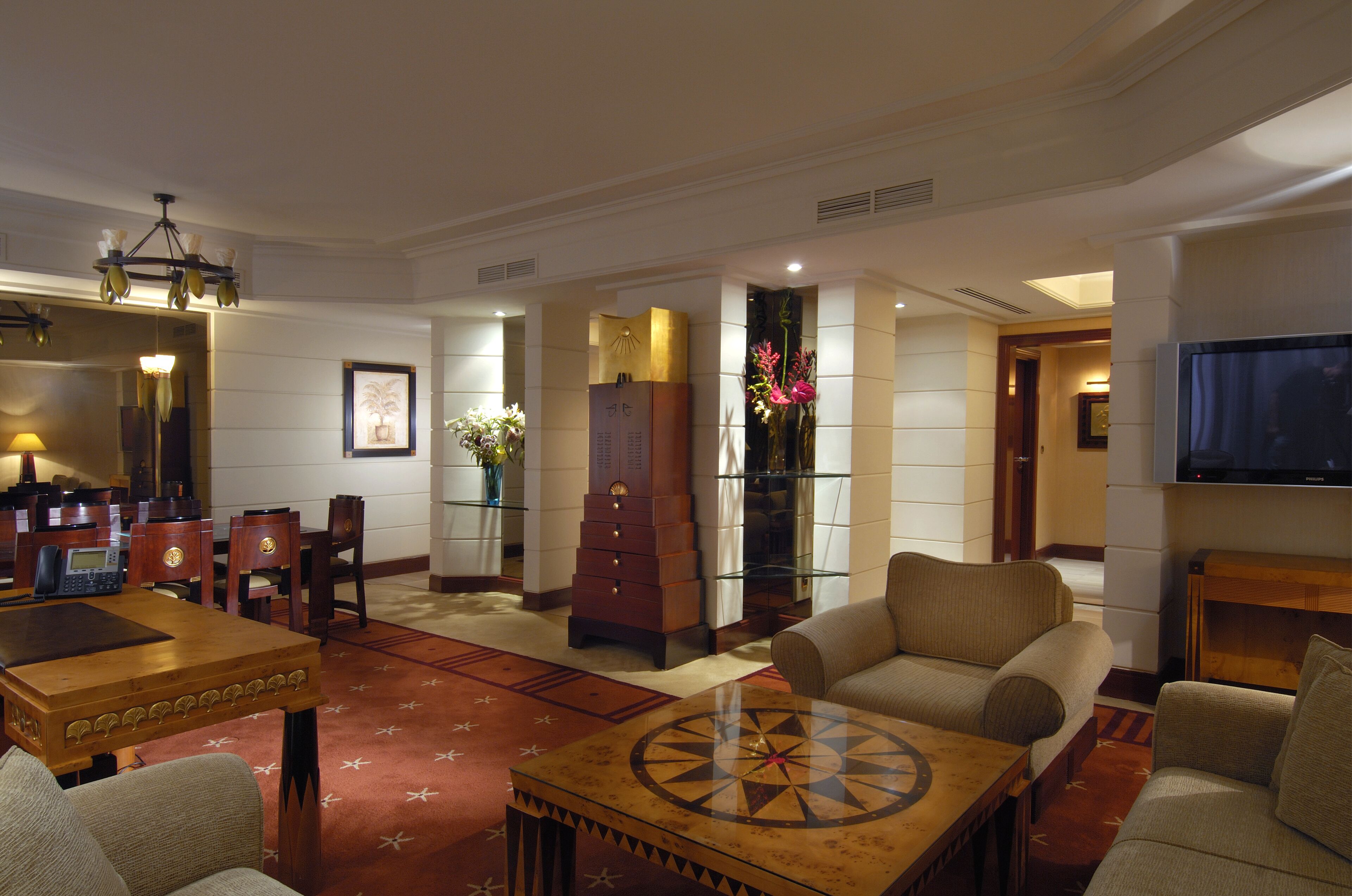 A hotel lobby with a wooden reception desk, a large clock, a television, and a seating area with sofas and a coffee table.