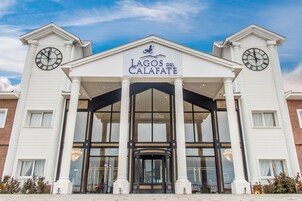 Una entrada de hotel con un acceso central, grandes puertas de cristal y un letrero que dice 'Lagos del Calafate'.