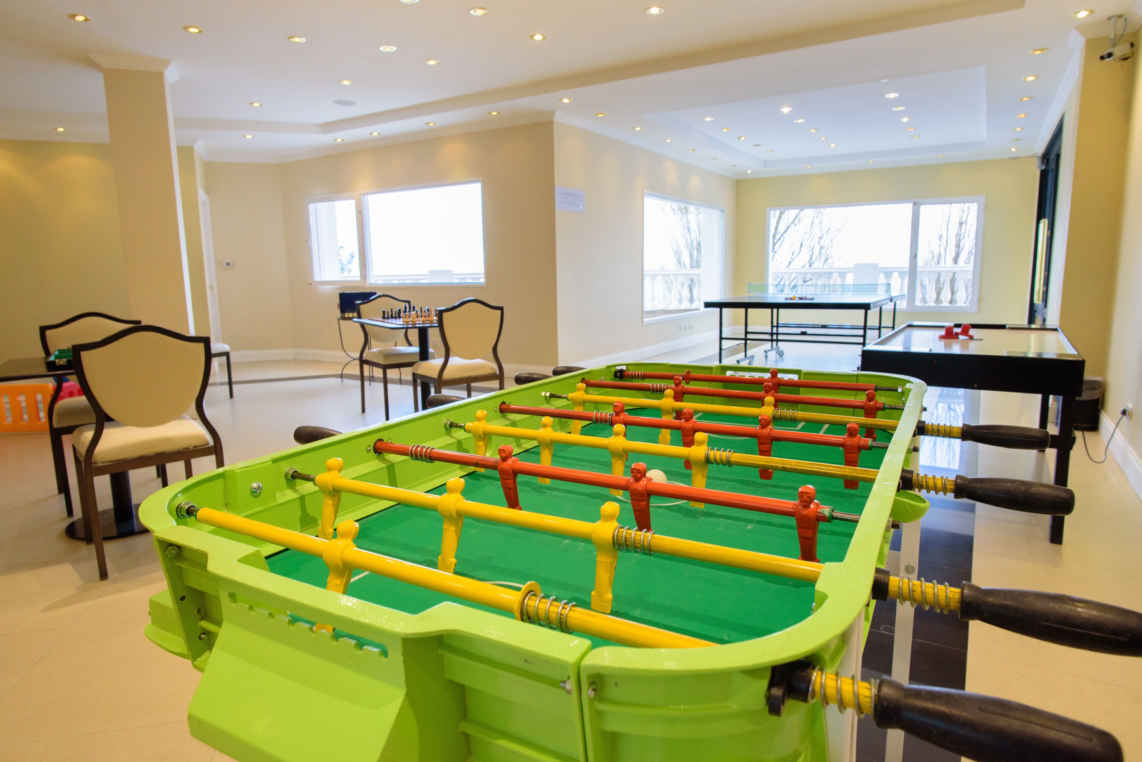 A room with a foosball table, a pool table, and a chess table.