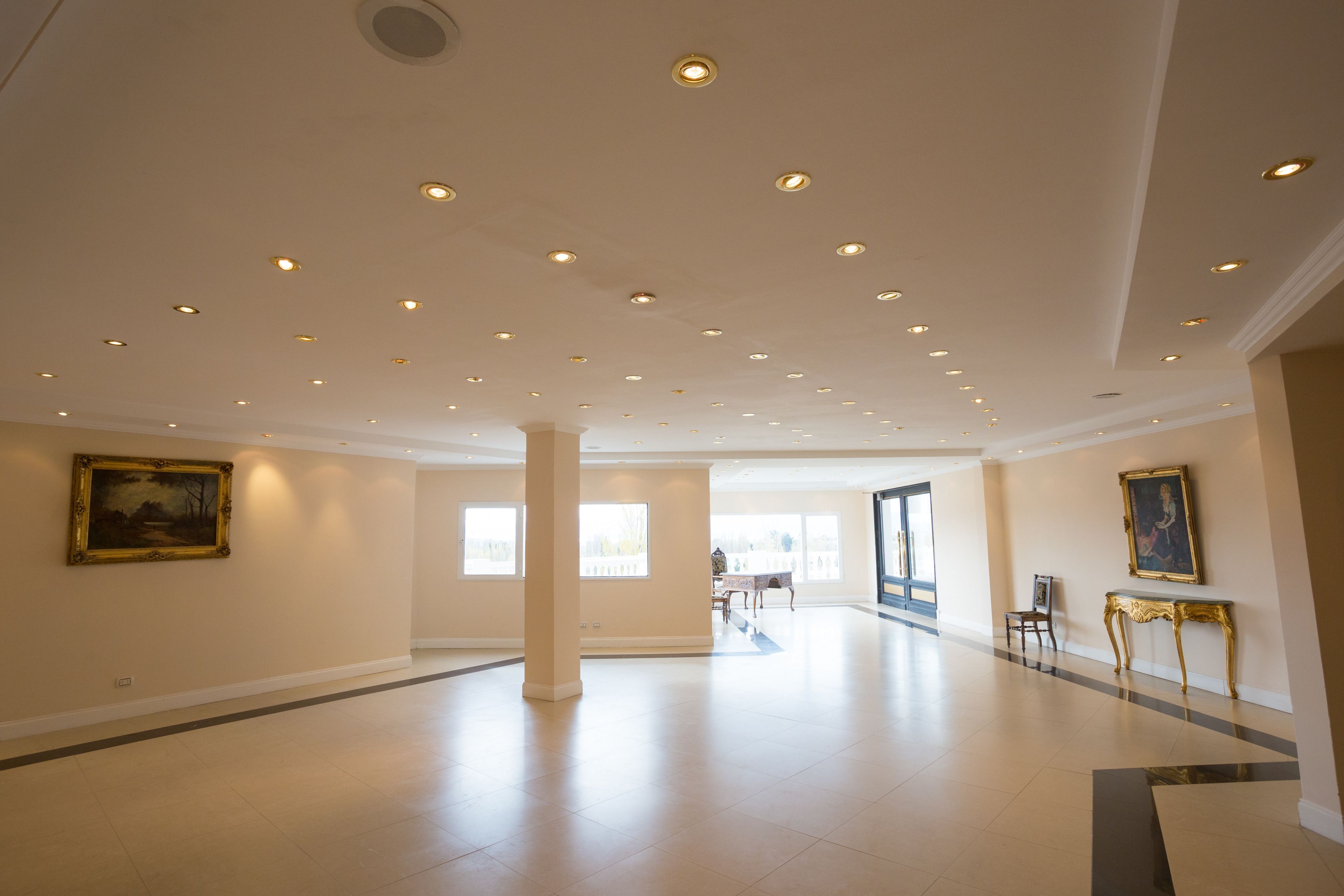 A spacious hotel lobby with a high ceiling, recessed lighting, and a few paintings on the walls.
