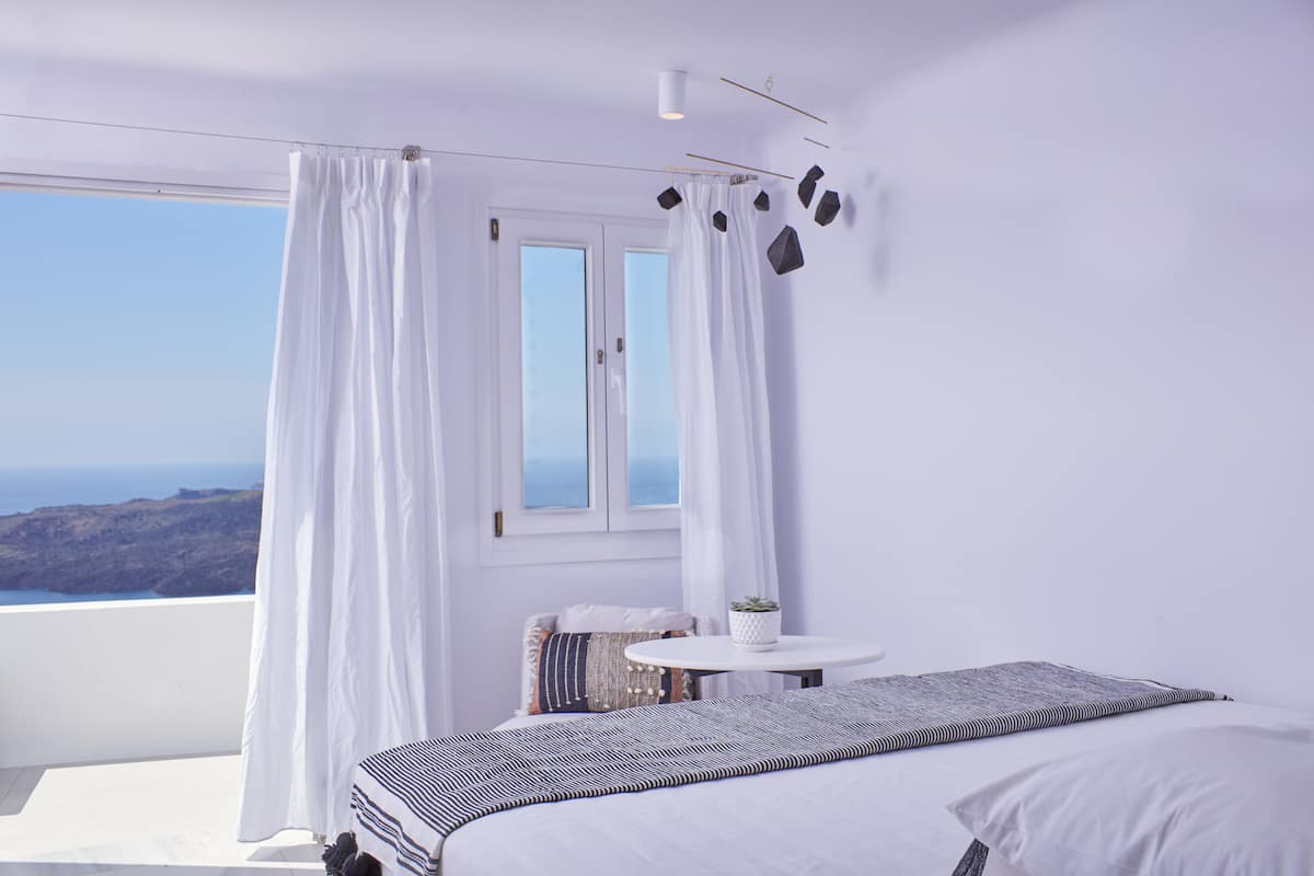 A bedroom with a large bed, a small round table, and a view of the sea.