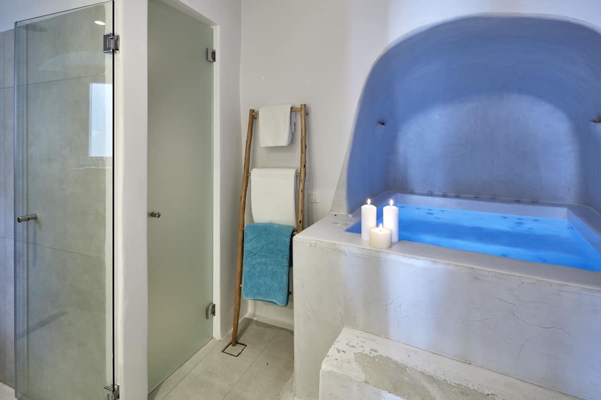 A bathroom with a glass shower enclosure, a bathtub with candles, and a wooden ladder.