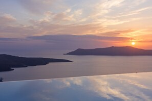 Un paisaje costero con un atardecer sobre el agua y colinas a lo lejos.